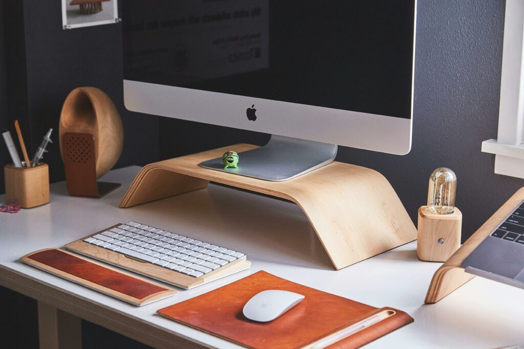 A modern home office desk setup featuring a Mac computer, a cell phone, pens, and a small plant, highlighting a clean and organized workspace.