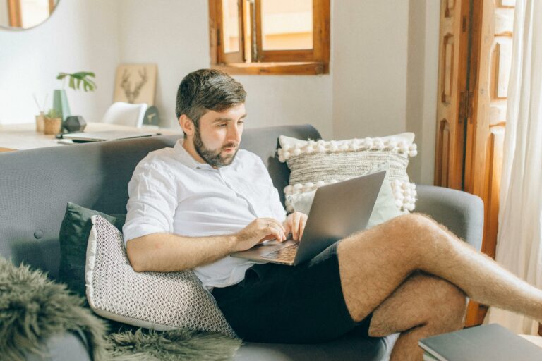 A man sitting on his couch using a laptop, illustrating the need for an improved home office setup.