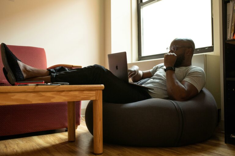 A man working on a laptop while sitting on a beanbag chair in a versatile and cozy home office space.