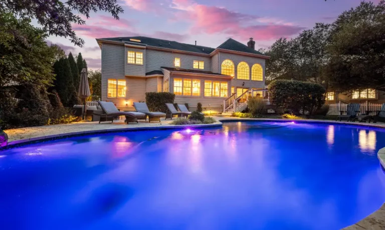 Backyard of Ashburn luxury home sold by top Realtors Jean Garrell Group, with a beautiful deep blue pool and exterior lighting at dusk